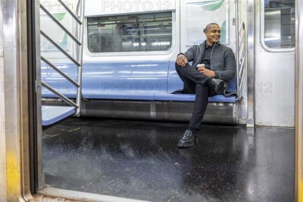 Man smiling and enjoying coffee while traveling on an empty subway car, reflecting daily commute, business lifestyle, and urban living within new york city