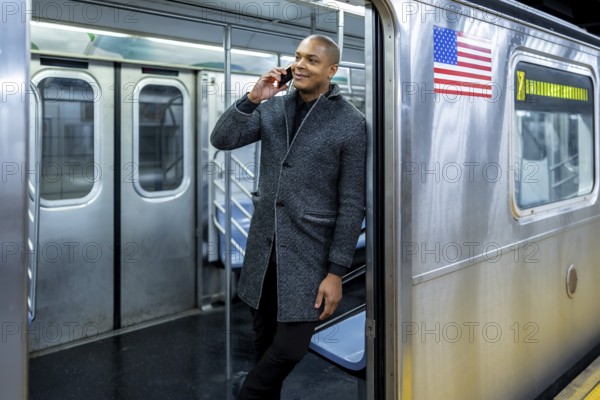 Smiling businessman traveling on a new york city subway train, talking on a mobile phone, representing urban professional life and connectivity during commute