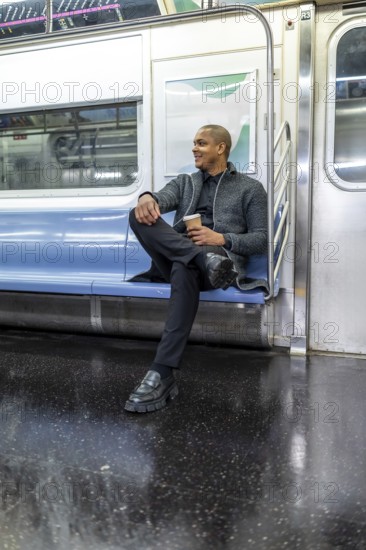 Young african american businessman on a new york city subway, seated with coffee cup, looking out thoughtfullystylish, confident commuter in smart casual attire during daily travel