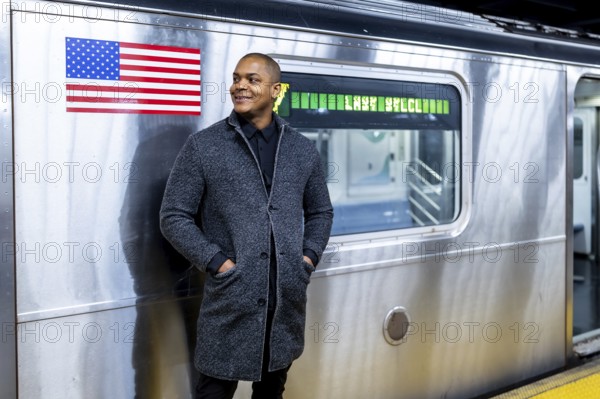 Young african american businessman standing on a subway platform in new york city, smiling while waiting for his train, symbolizing urban lifestyle, commute, and ambition