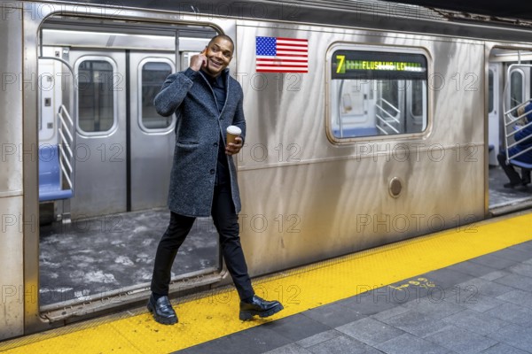 Young professional in a winter coat walks a manhattan subway platform, holding coffee and talking on a smartphone beside a waiting 7 train during a busy commute