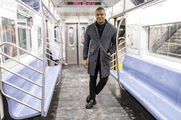 Young man standing inside an empty manhattan subway car, dressing in smart casual attire, smiling at the camera, and representing urban life and daily transit