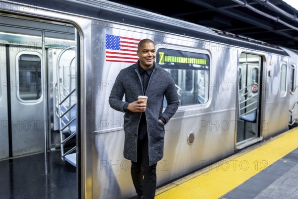 African american professional standing on a manhattan subway platform holding a coffee cup and looking away as an open train waits, urban commuter scene conveying ambition and motion