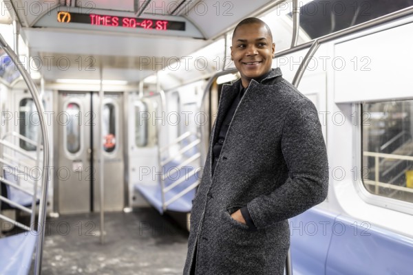 Happy black businessman standing inside an nearly empty new york subway car, smiling as he commutes through manhattan to a business meeting, confident and stylish in coat and suit