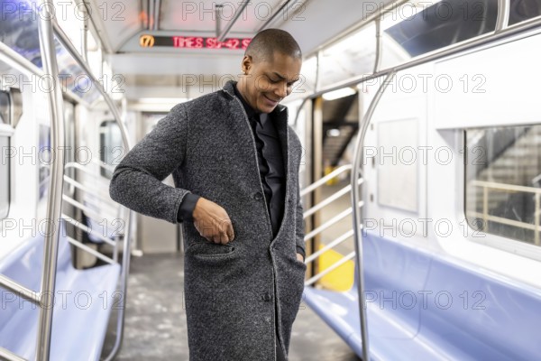 Young professional standing in a manhattan subway car, smiling as he adjusts his coat pocket, ready for a busy day of commuting and work in the urban morning bustle