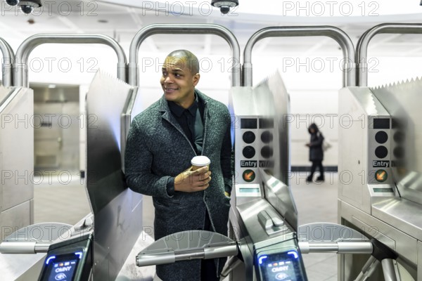 Professional man carrying a coffee cup, about to enter the subway system through modern turnstiles, representing urban commuting and daily routine in a metropolitan city