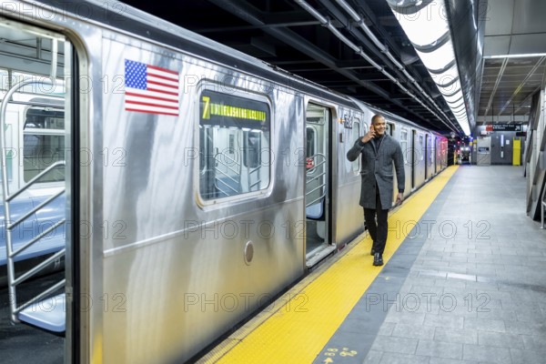 Professional businessman smiling and talking on his phone while exiting a manhattan subway train, walking the busy underground platform during an urban commute and business trip