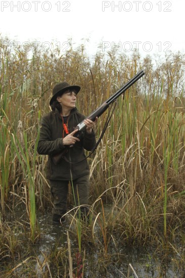 Female hunter standing in water with hunting rifle and eagerly waiting for flying ducks, Allgäu, Bavaria, Germany, Allgäu, Bavaria, Germany