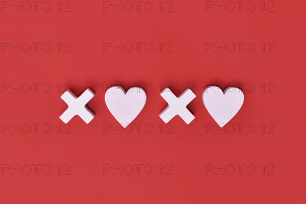 Valentine flat lay with wooden light pink hearts and XOXO letters arranged on a red background. Love, hugs and kisses holiday message