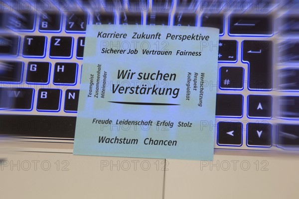 (Added) Text WE ARE LOOKING FOR REINFORCEMENT, surrounded by positive terms such as career, future, team spirit, trust, appreciation, growth and opportunities on a piece of paper lying on a laptop