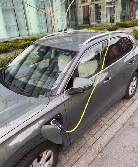 An e-car is charged at a charging station in Düsseldorf, the charging cable is stored over the roof of the car, Düsseldorf, Germany