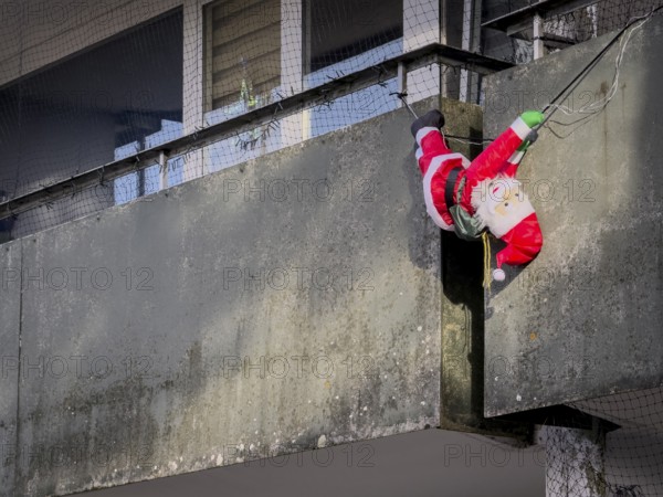 A Santa Claus figure hangs on a concrete balcony behind fir trees, Wuppertal, Germany