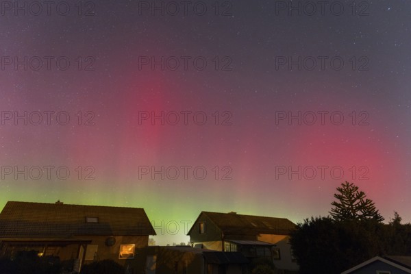 Northern lights in the night sky above houses, shimmering red and green, accompanied by sparkling stars, aurora borealis, Ilsede, Lower Saxony, Germany