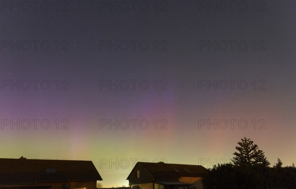 Shimmering purple and green auroras in the evening sky above residential buildings, aurora borealis, Ilsede, Lower Saxony, Germany