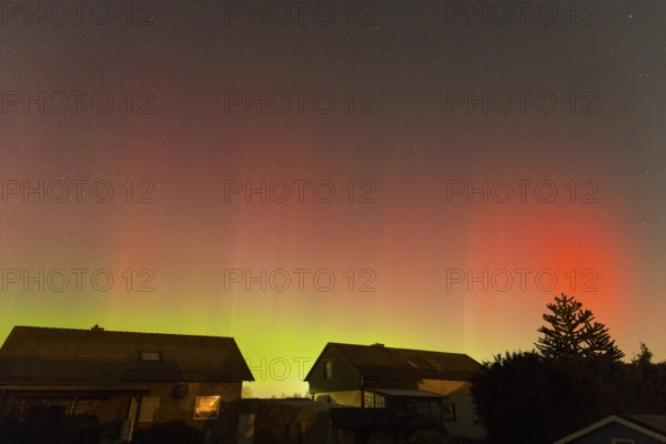 Red-green auroras illuminate the evening sky over residential buildings, aurora borealis, Ilsede, Lower Saxony, Germany