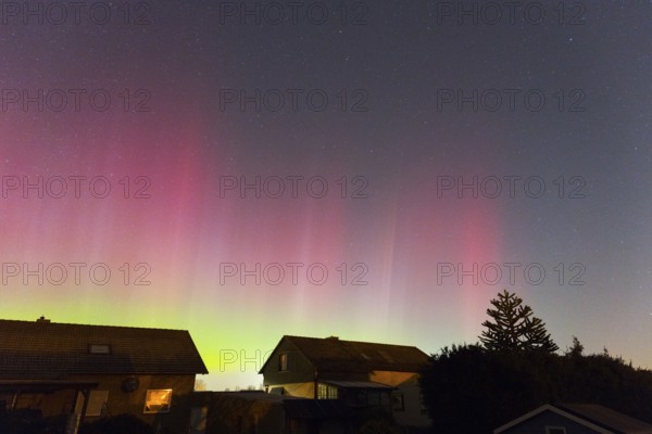 Intense red and green aurora glowing above the houses in the evening sky, aurora borealis, Ilsede, Lower Saxony, Germany