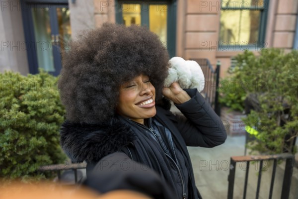 Young black woman with a big afro hairstyle taking a selfie, enjoying a sunny winter day in manhattan and showing natural beauty and happiness in an urban environment