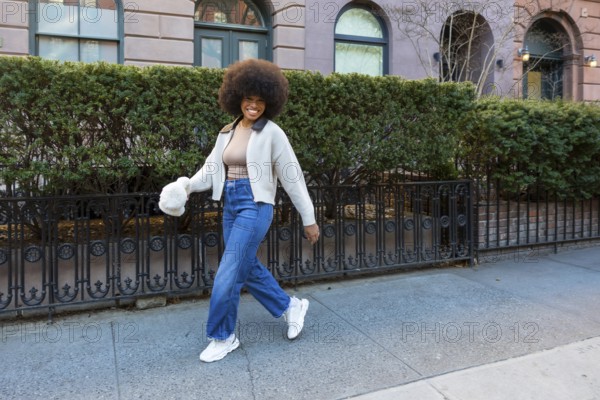 Happy young black woman with afro confidently walking manhattan streets, smiling and enjoying vibrant urban lifestyle in casual denim and sneakers, radiating freedom and positive energy