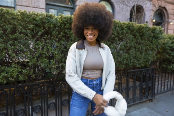 Joyful young black woman with a natural afro hairstyle walking and smiling confidently on a street in manhattan, new york city, embracing individuality and urban fashion