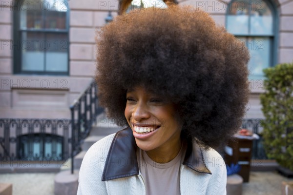 Cheerful young african american woman with a large afro hairstyle smiling genuinely, exuding joy and self acceptance while standing outdoors in a new york city neighborhood