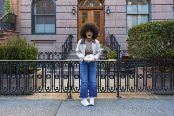 Cheerful smiling woman standing on a new york city street, holding white yarn in her hands, reflecting urban life and creativity in an authentic moment