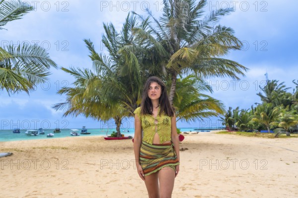 Woman standing on a sandy beach looking out towards the turquoise ocean, surrounded by lush palm trees and local boats, capturing the essence of a serene tropical getaway