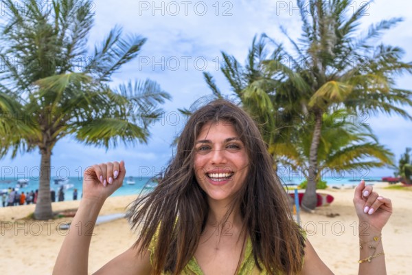 Young woman smiling with joy, celebrating her tropical beach vacation with swaying palm trees and turquoise ocean in the background, a perfect moment of happiness and relaxation