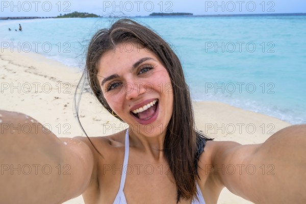 Woman smiling for a selfie on a white sand maldivian beach, embracing sunny tropical vacation vibes with turquoise ocean, blue sky and carefree summer joy