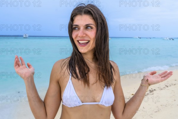 Young woman smiling and gesturing excitedly, experiencing joy and freedom during a relaxing summer holiday surrounded by turquoise ocean and white sand