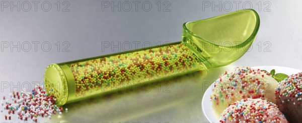 Yellow, transparent ice cream scoop filled with coloured sugar sprinkles, next to a plate with different types of ice cream, decorated with coloured sugar sprinkles