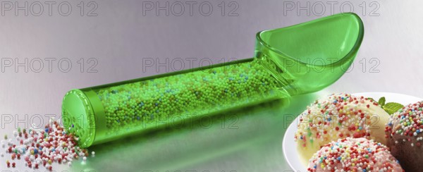 Green, transparent ice cream scoop filled with coloured sugar sprinkles, next to plates with different types of ice cream, decorated with coloured sugar sprinkles