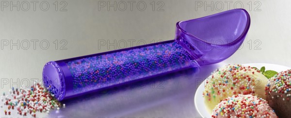 Purple, transparent ice cream scoop filled with coloured sugar sprinkles, next to plates with different types of ice cream, decorated with coloured sugar sprinkles