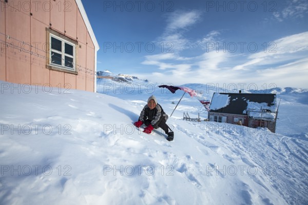 A child playing in the snow in Tiniteqilaaq. Tiniteqilaaq is one of the five settlements in the area around Ammassalik Island, located in the Sermersooq municipality on Ikasativaq Fjord, north of Ammassalik Island and facing Sermilik, Greenland, North America