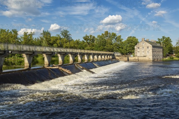 Moulin Neuf water flow control dam and walkway over Des Mille-Iles river plus New Mill on Ile des Moulins in summer, Old Terrebonne, Quebec, Canada