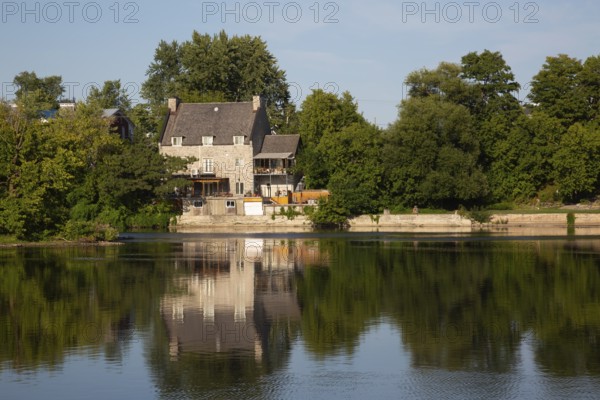 19th century multistory old cut stone home with weathered cedar shingles roof and backyard built on edge of Des Mille-Iles River in summer, Terrebonne, Quebec, Canada