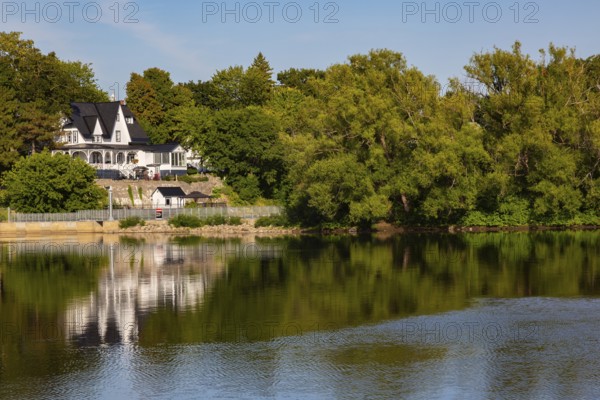 19th century multistory old white clapboard home with black rooftops and backyard built on edge of Des Mille-Iles River in summer, Terrebonne, Quebec, Canada