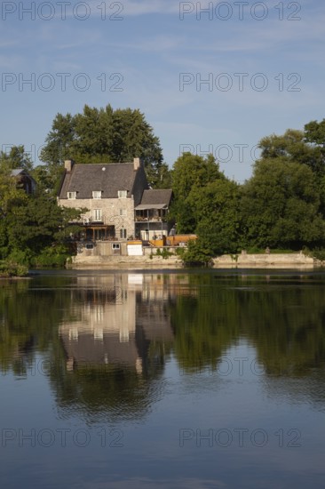 19th century multistory old cut stone home with weathered cedar shingles roof and backyard built on edge of Des Mille-Iles River in summer, Terrebonne, Quebec, Canada
