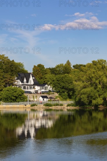 19th century multistory old white clapboard home with black rooftops and backyard built on edge of Des Mille-Iles River in summer, Terrebonne, Quebec, Canada