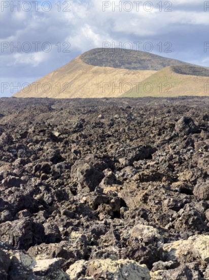 Hiking trail through lava rock to Caldera Blanca volcano against blue sky with white clouds, Mancha Blanca, Lanzarote, Canary Islands, Spain