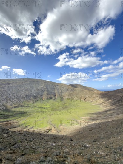 View of the Caldera Blanca volcano cauldron against blue sky with white clouds, Mancha Blanca, Lanzarote, Canary Islands, Spain