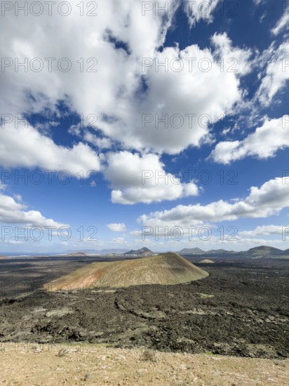 View from Caldera Blanca volcano to Caldereta against blue sky with white clouds, Mancha Blanca, Lanzarote, Canary Islands, Spain