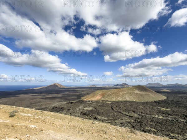 View from Caldera Blanca volcano to Caldereta against blue sky with white clouds, Mancha Blanca, Lanzarote, Canary Islands, Spain