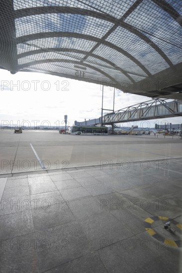 View of the apron of an airport with a bus and a mesh roof in bright sunlight, Stuttgart Airport, Germany