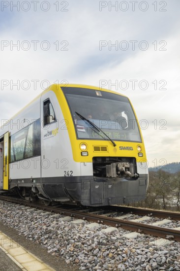 A train travels head-on on rails through rural areas under a cloudy sky, taking off the Hermann Hessebahn, Calw, Germany