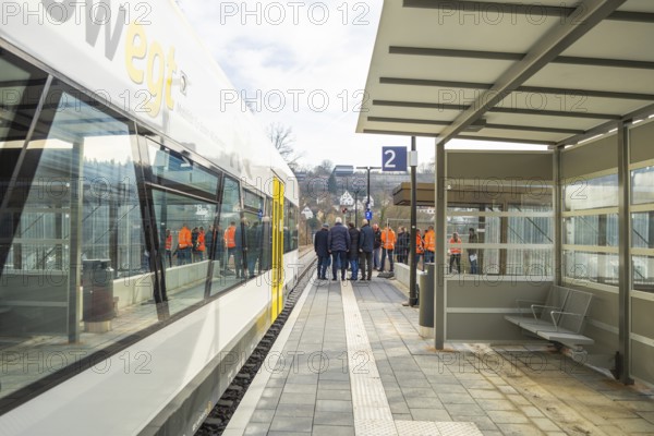 People standing in a group on a platform next to a train at a bus stop, the Hermann Hessebahn ride, Calw, Germany
