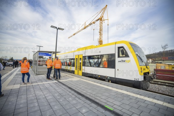 People standing on the platform next to a train and a construction crane in cloudy skies, the Hermann Hessebahn, Calw, Germany