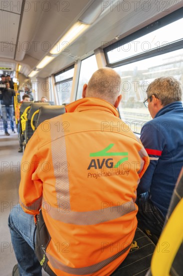 Back view of men on a train, one wearing an AVG work jacket, taking off the Hermann Hessebahn, Calw, Germany