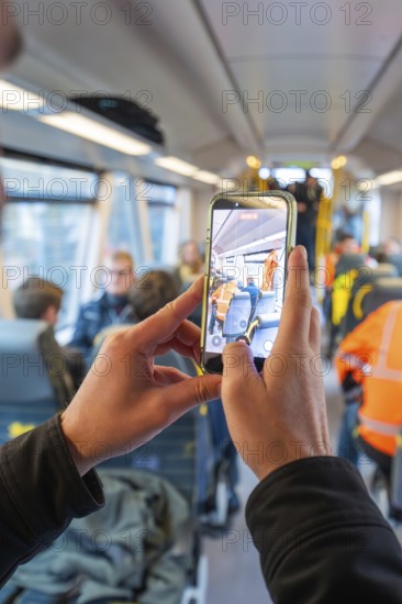 Man taking a photo with a smartphone in a busy train interior, taking the Hermann Hessebahn, Calw, Germany