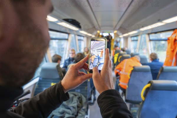 Person photographs the interior of a train and other passengers with a smartphone, Hermann Hessebahn's journey, Calw, Germany