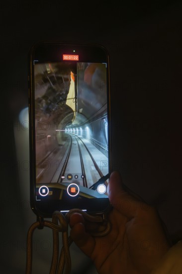 A smartphone shows the inside view of a tunnel crossed by a train, held by one hand, the Hermann Hessebahn, Calw, Germany